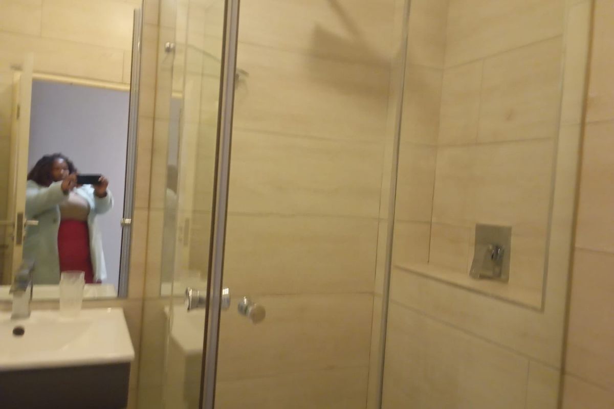 A modern bathroom featuring a glass-enclosed shower with wall-mounted fixtures and a vanity basin with a mirror.