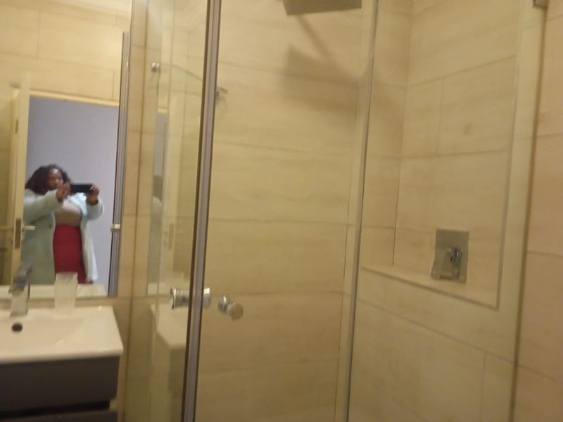 A modern bathroom featuring a glass-enclosed shower with wall-mounted fixtures and a vanity basin with a mirror.