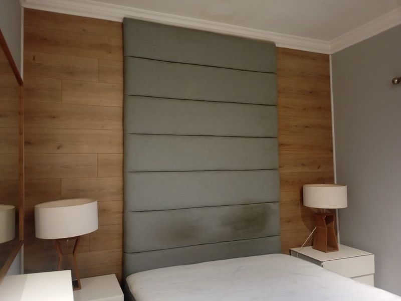 Bedroom featuring a wood-paneled accent wall and a tall upholstered headboard with integrated bedside lighting.