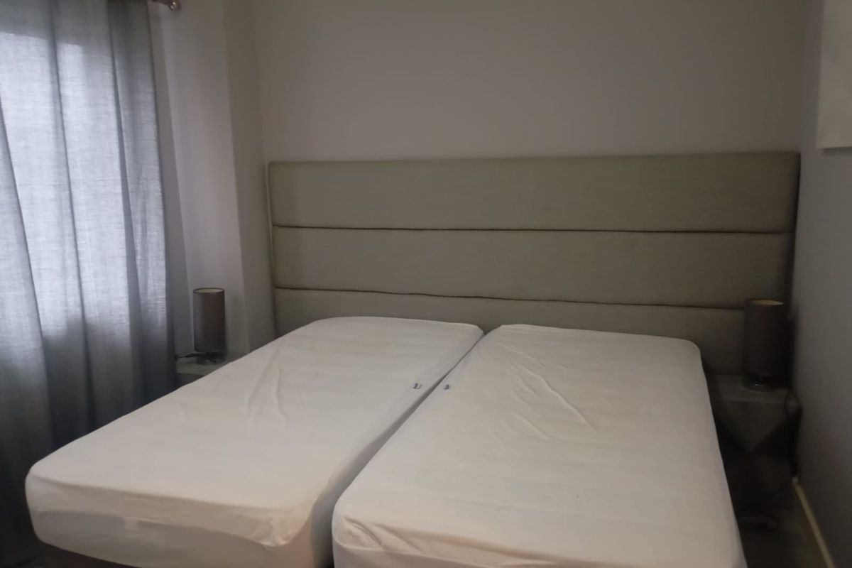 A bedroom featuring a neutral wall-mounted headboard and window with grey curtains.