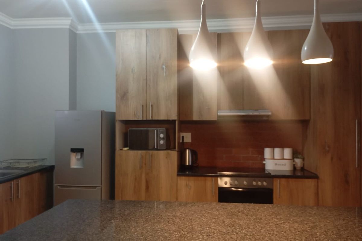 Modern kitchen featuring wood-look cabinetry, granite countertops, a built-in oven, extractor fan, and stylish pendant lighting over a central island.