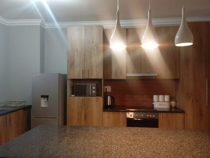 Modern kitchen featuring wood-look cabinetry, granite countertops, a built-in oven, extractor fan, and stylish pendant lighting over a central island.
