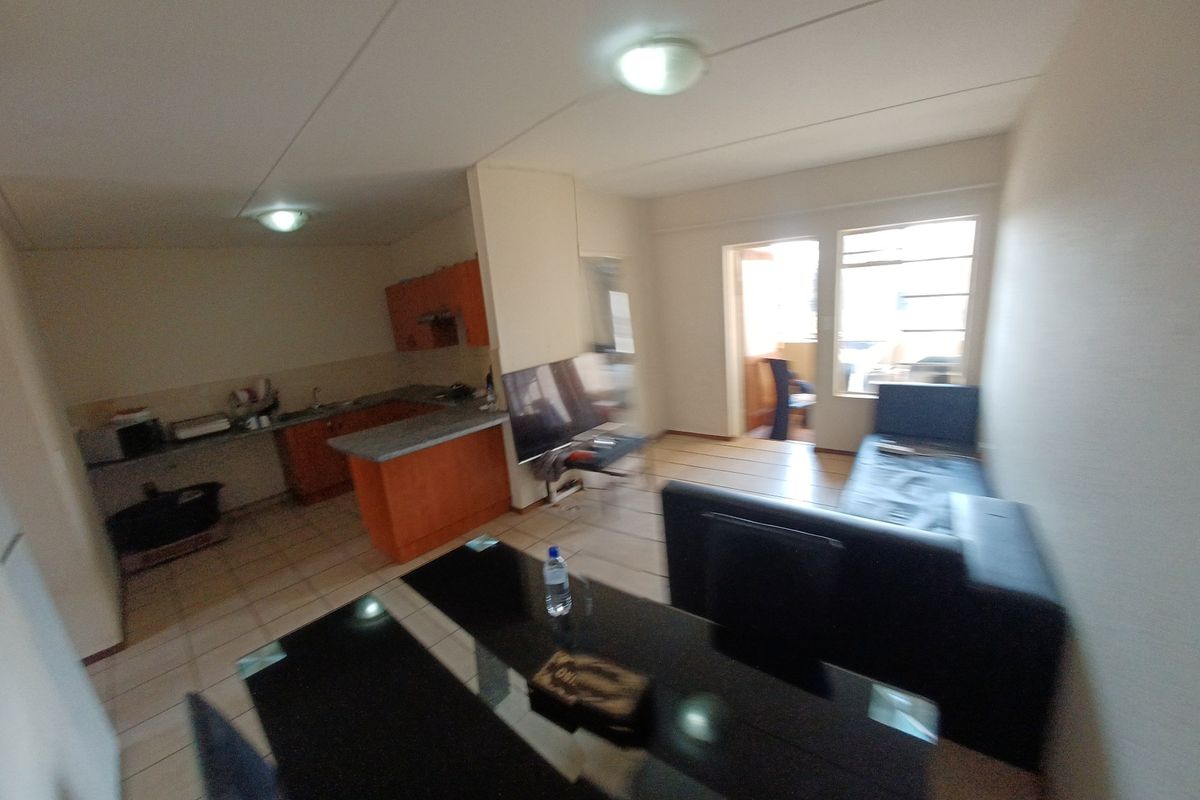 Open-plan living area featuring a kitchen with built-in cabinetry and tiled flooring, leading to an adjacent balcony space.