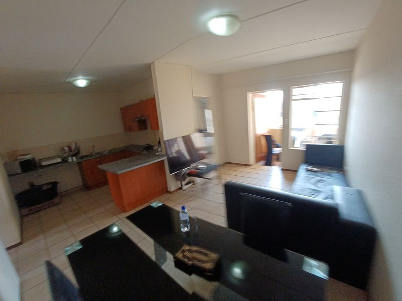Open-plan living area featuring a kitchen with built-in cabinetry and tiled flooring, leading to an adjacent balcony space.