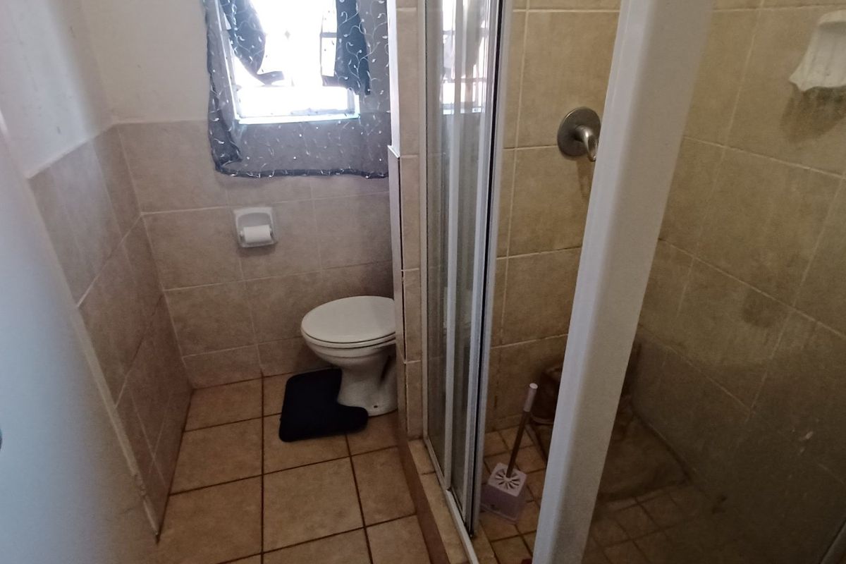 A functional bathroom featuring a shower enclosure, toilet, and neutral wall and floor tiling.