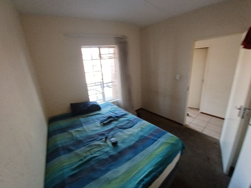A simple bedroom featuring carpeted flooring and a window, providing access to an adjacent hallway area.
