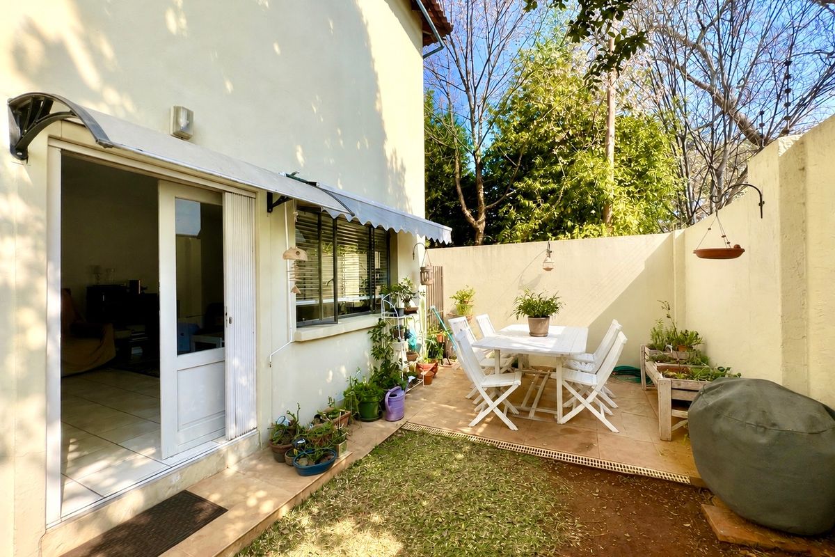 A private rear courtyard featuring a tiled patio area, retractable awning, and secure boundary walls with electric fencing, accessible via a sliding door.