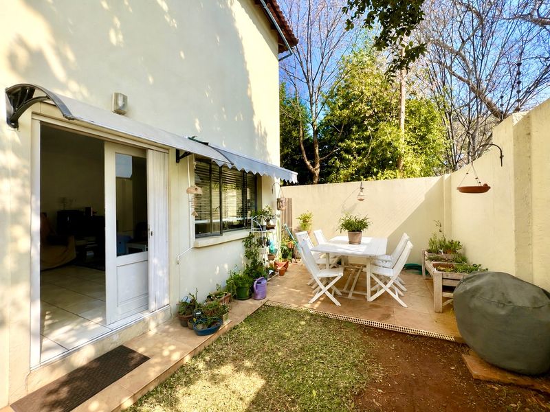 A private rear courtyard featuring a tiled patio area, retractable awning, and secure boundary walls with electric fencing, accessible via a sliding door.
