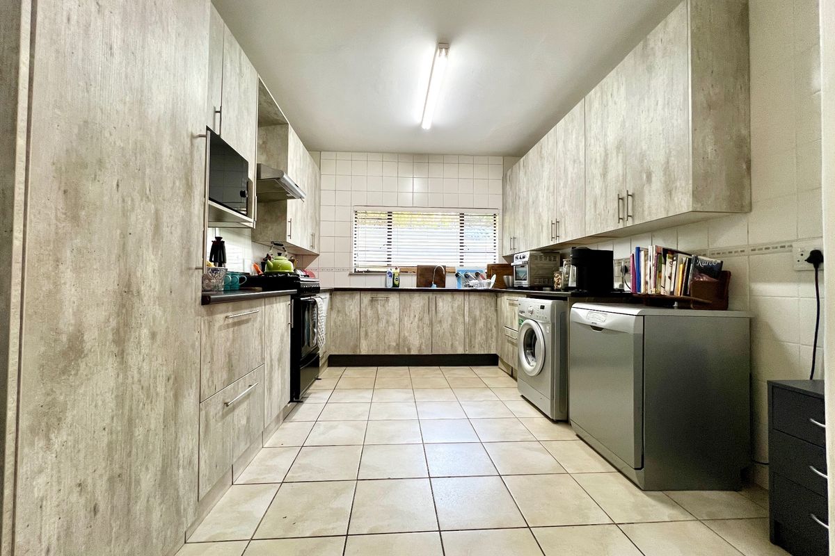 A functional galley-style kitchen featuring wood-look laminate cabinetry, tiled flooring, a tiled backsplash, and integrated appliance spaces.