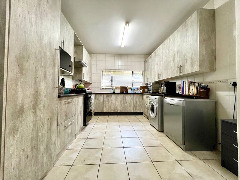 A functional galley-style kitchen featuring wood-look laminate cabinetry, tiled flooring, a tiled backsplash, and integrated appliance spaces.