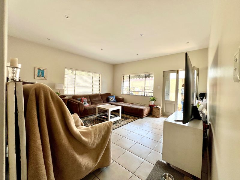 A spacious living room featuring neutral tiled flooring, recessed downlighting, and natural light provided by multiple windows and a glass panel door.