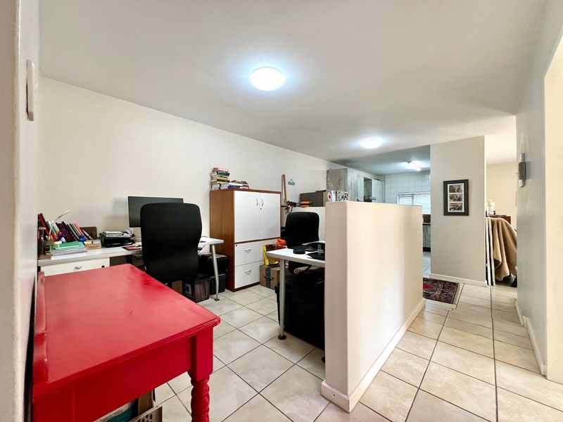 An open-plan living area featuring tiled flooring and a central partition wall, providing a versatile space that flows into the kitchen area.