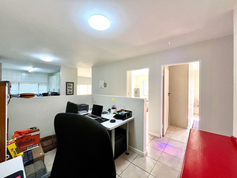 A functional office space featuring tiled flooring, flush mount lighting, and a half-height partition wall, providing a semi-private work area within the apartment.