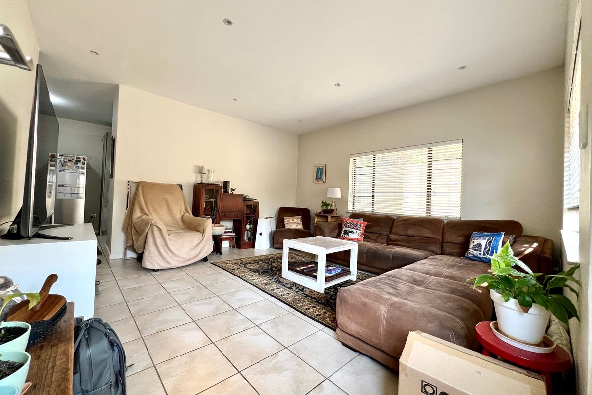 A spacious living room featuring neutral tiled flooring, recessed downlighting, and large windows fitted with venetian blinds, offering a comfortable and functional living space.