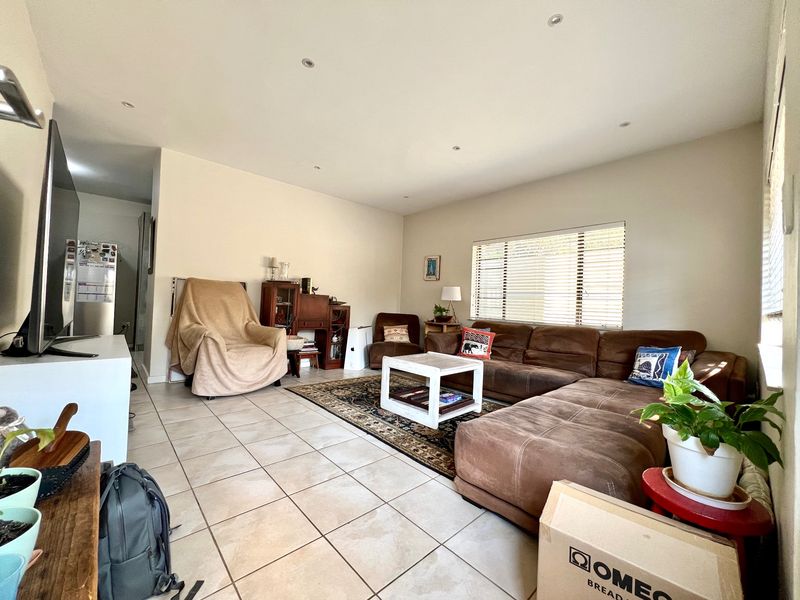 A spacious living room featuring neutral tiled flooring, recessed downlighting, and large windows fitted with venetian blinds, offering a comfortable and functional living space.