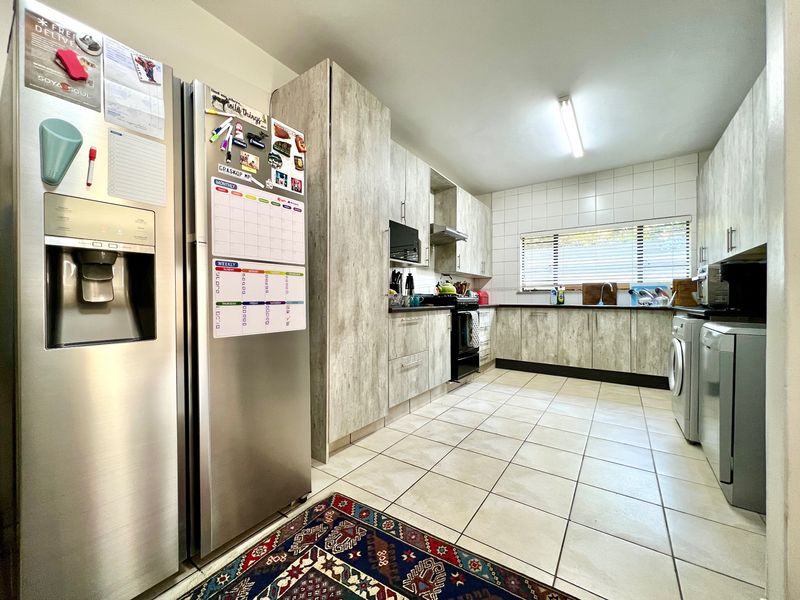 A functional kitchen featuring light wood-look cabinetry, tiled flooring, a tiled backsplash, and integrated appliances with ample counter space.