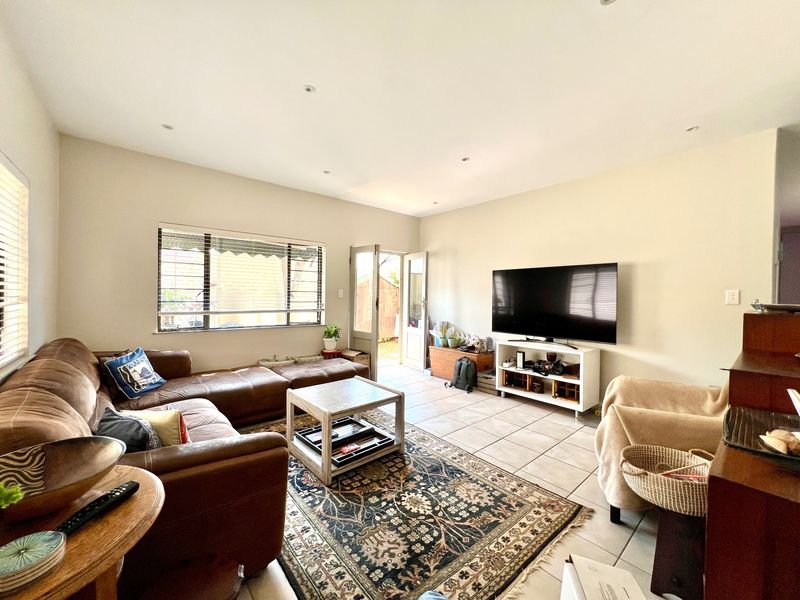 A spacious living room featuring tiled flooring, recessed lighting, and direct access to an outdoor area through a glass panel door.