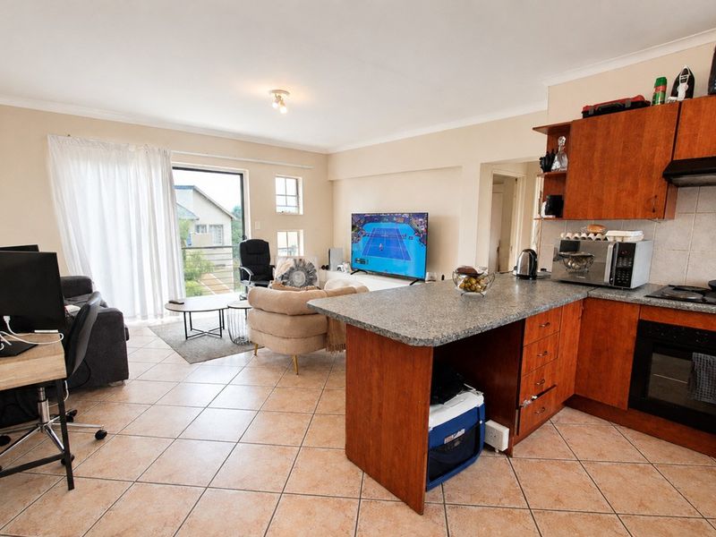 Open-plan living area featuring a kitchen with laminate cabinetry, built-in oven, and hob, flowing into a lounge space with access to a balcony.