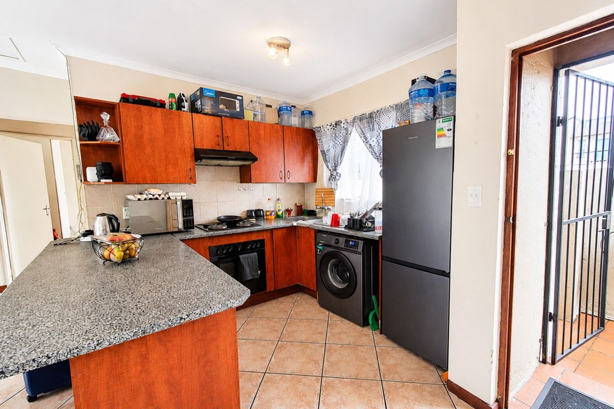 Functional kitchen featuring laminate cabinetry, granite-look countertops, built-in oven, hob, and extractor fan, with direct access to an exterior security gate.
