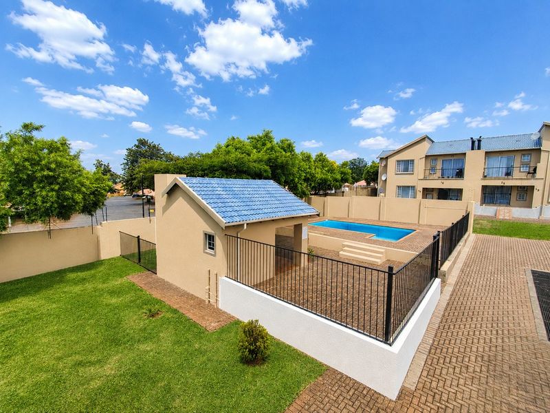 Outdoor entertainment area featuring a swimming pool, paved surround, and a lapa structure within a secure, fenced complex setting.