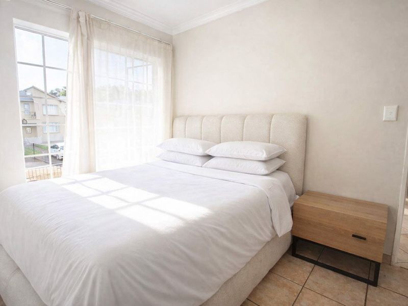 A bright and well-maintained bedroom featuring tiled flooring, neutral walls, and a large window allowing for ample natural light.