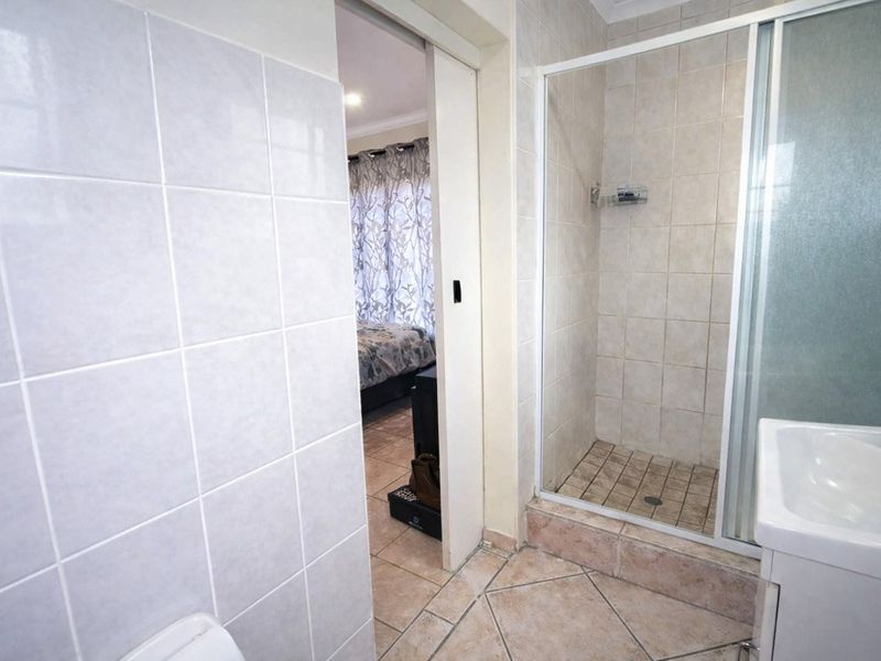 A functional bathroom featuring a shower enclosure, tiled walls and flooring, and a vanity basin, with a sliding door leading to the adjacent bedroom.