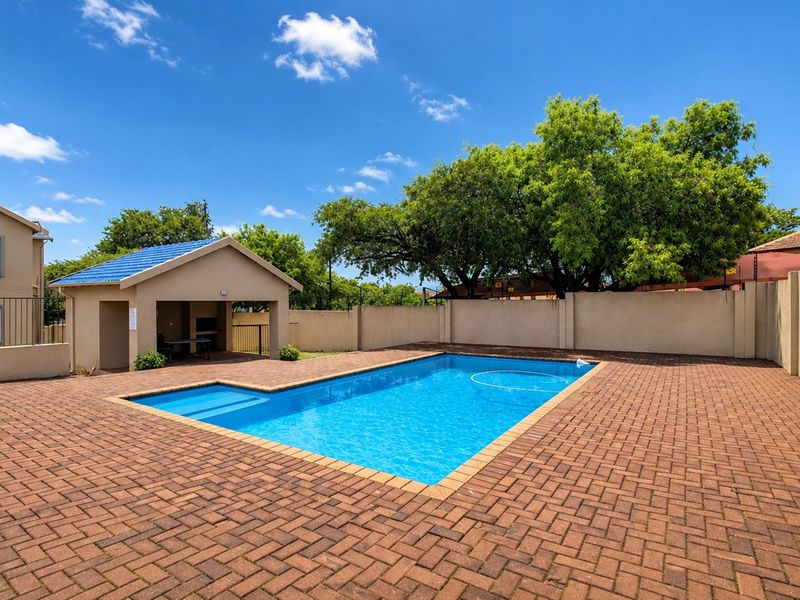 Communal pool area featuring a paved deck, perimeter walling, and a covered entertainment structure with a built-in braai facility.