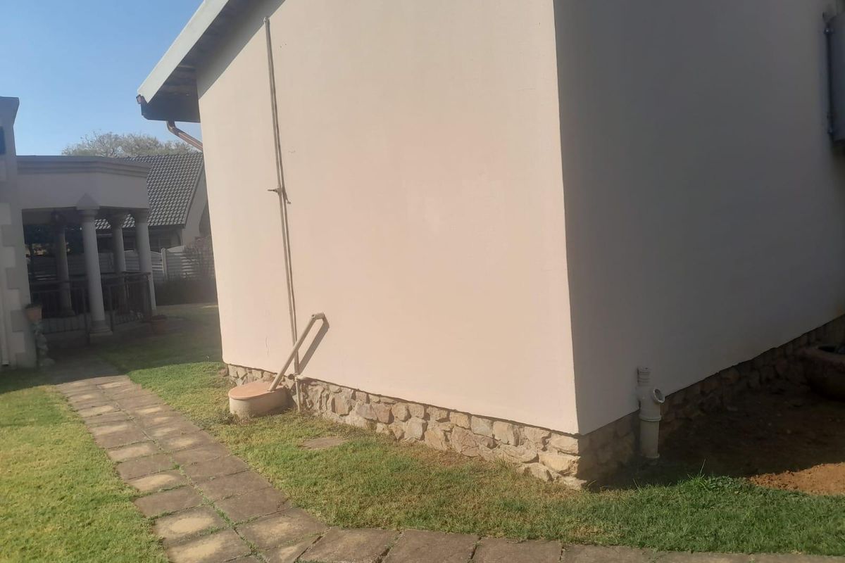 A view of the rear exterior wall featuring stone cladding at the base, a paved walkway, and external plumbing fixtures.