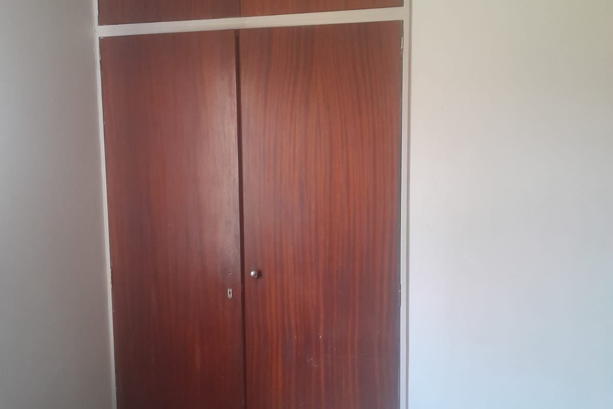 A bedroom featuring a full-height built-in wooden wardrobe with integrated overhead storage cupboards.