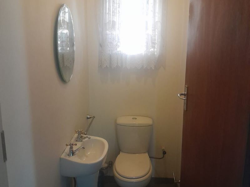 A compact guest bathroom featuring a pedestal basin and toilet with tiled flooring and natural light from a window.