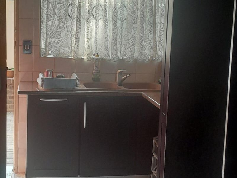 A functional kitchen area featuring dark built-in cabinetry, a double sink with mixer tap, and tiled flooring with a tiled splashback.