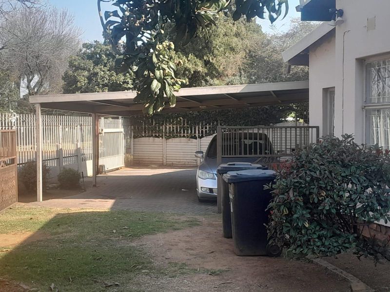 Front exterior view showing a paved driveway, covered carport, and perimeter security fencing.