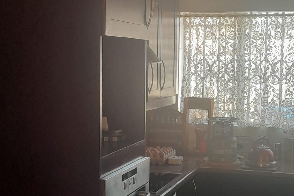 A compact kitchen featuring dark built-in cabinetry, a built-in oven, and a functional countertop workspace with natural light from the window.