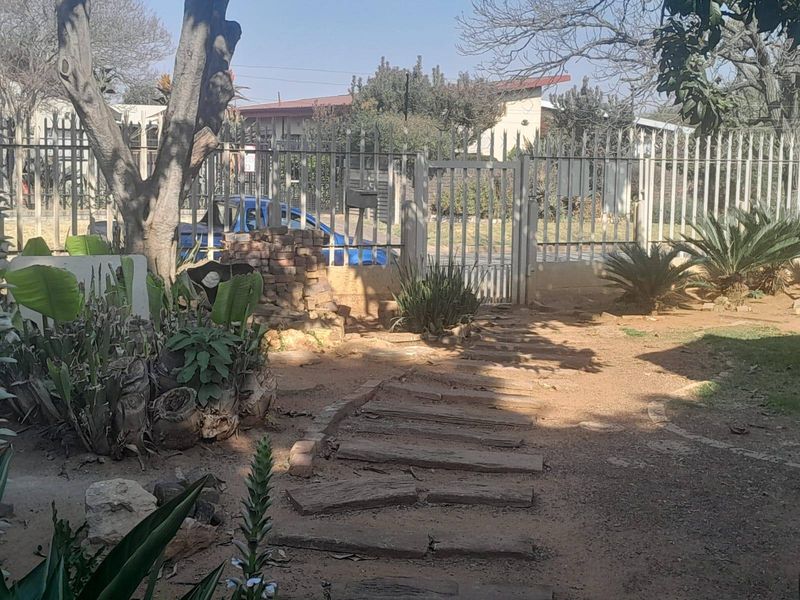 Front garden area featuring a metal security fence, pedestrian gate, and a stone pathway leading toward the property entrance.