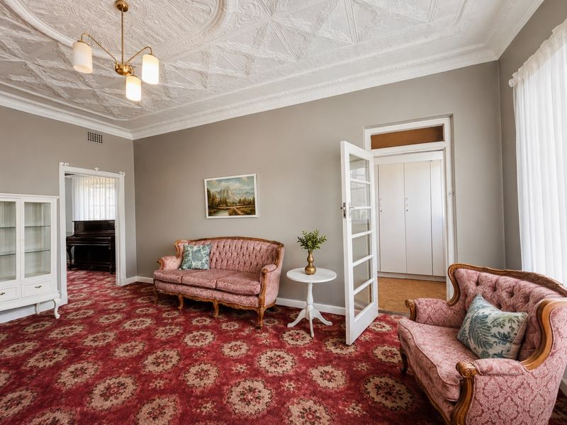 Spacious living room featuring an ornate plaster ceiling, classic coving, and a glass-paneled french door leading to an adjacent room with built-in storage.