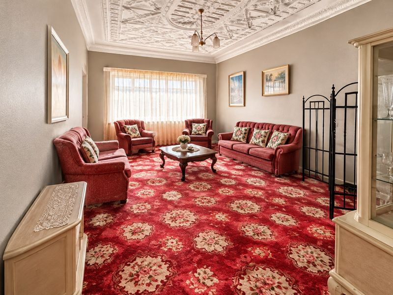 Spacious living room featuring an ornate plaster ceiling, coving, and large windows, offering a classic aesthetic with potential for modern updates.