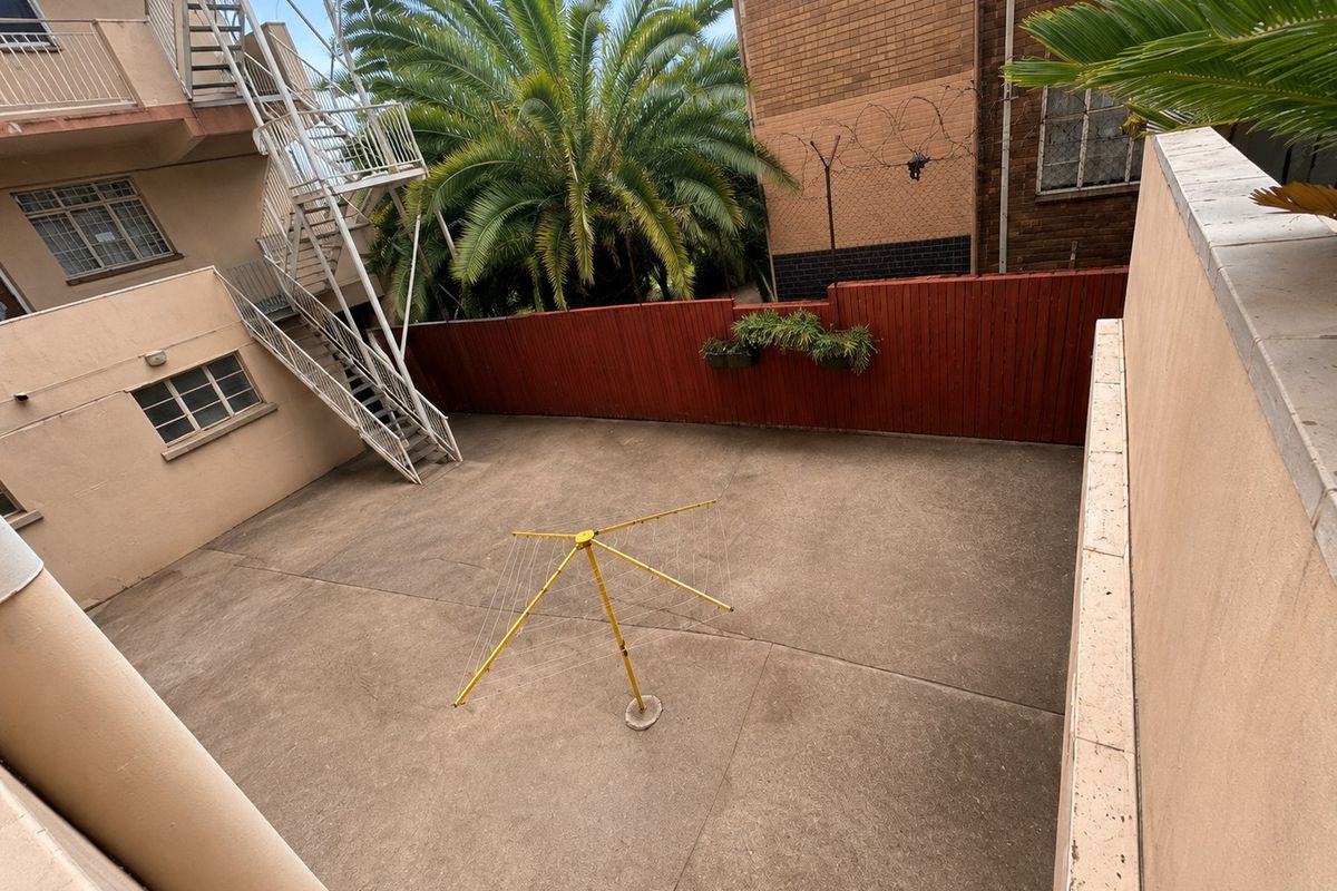 A paved rear courtyard area featuring a metal fire escape staircase, timber boundary fencing, and security razor wire.