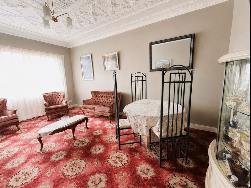 A spacious living room featuring an ornate plaster ceiling, coving, and large windows, currently finished with traditional patterned carpeting.
