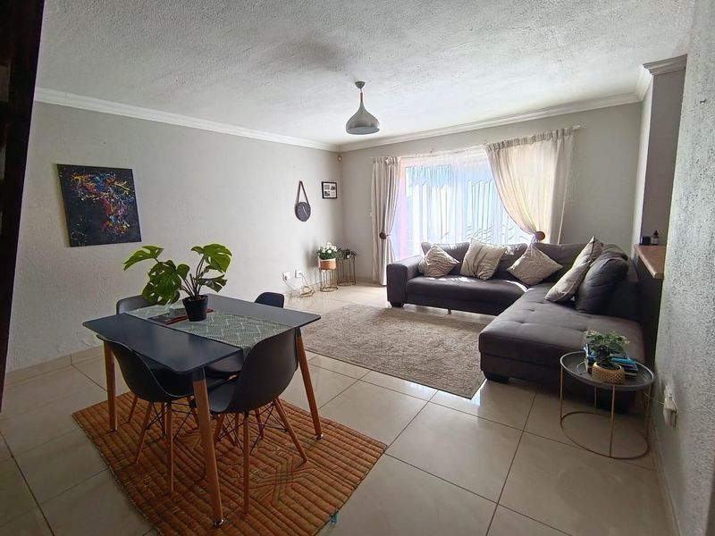 An open-plan living and dining area featuring neutral wall tones, large format floor tiles, and a sliding glass door providing natural light.