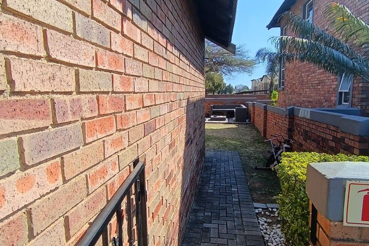 A side walkway featuring brick paving leading to a rear garden area, enclosed by brick boundary walls and a metal gate.