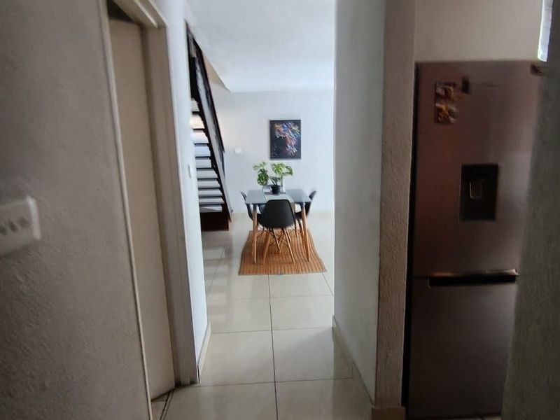 A view through a tiled hallway leading towards a dining area and staircase, featuring neutral wall finishes and classic cornicing.
