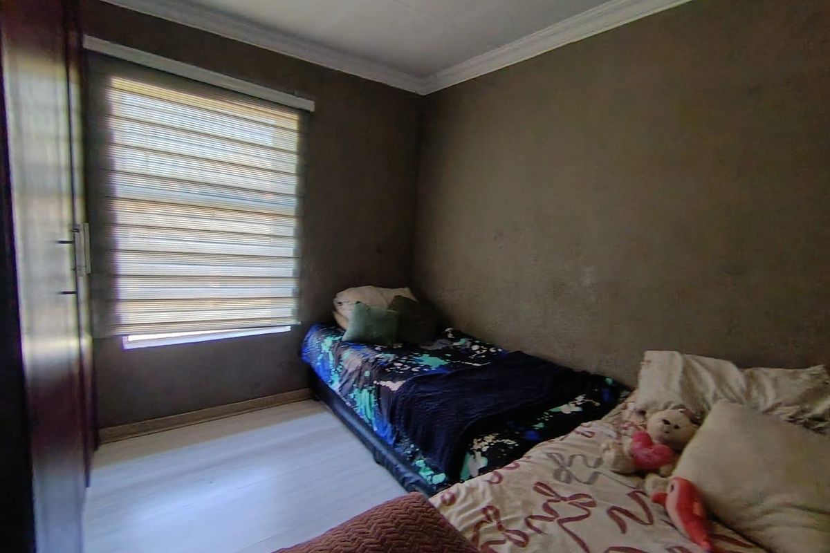 A bedroom featuring laminate flooring, built-in cupboards, and roller blinds, with neutral wall finishes.