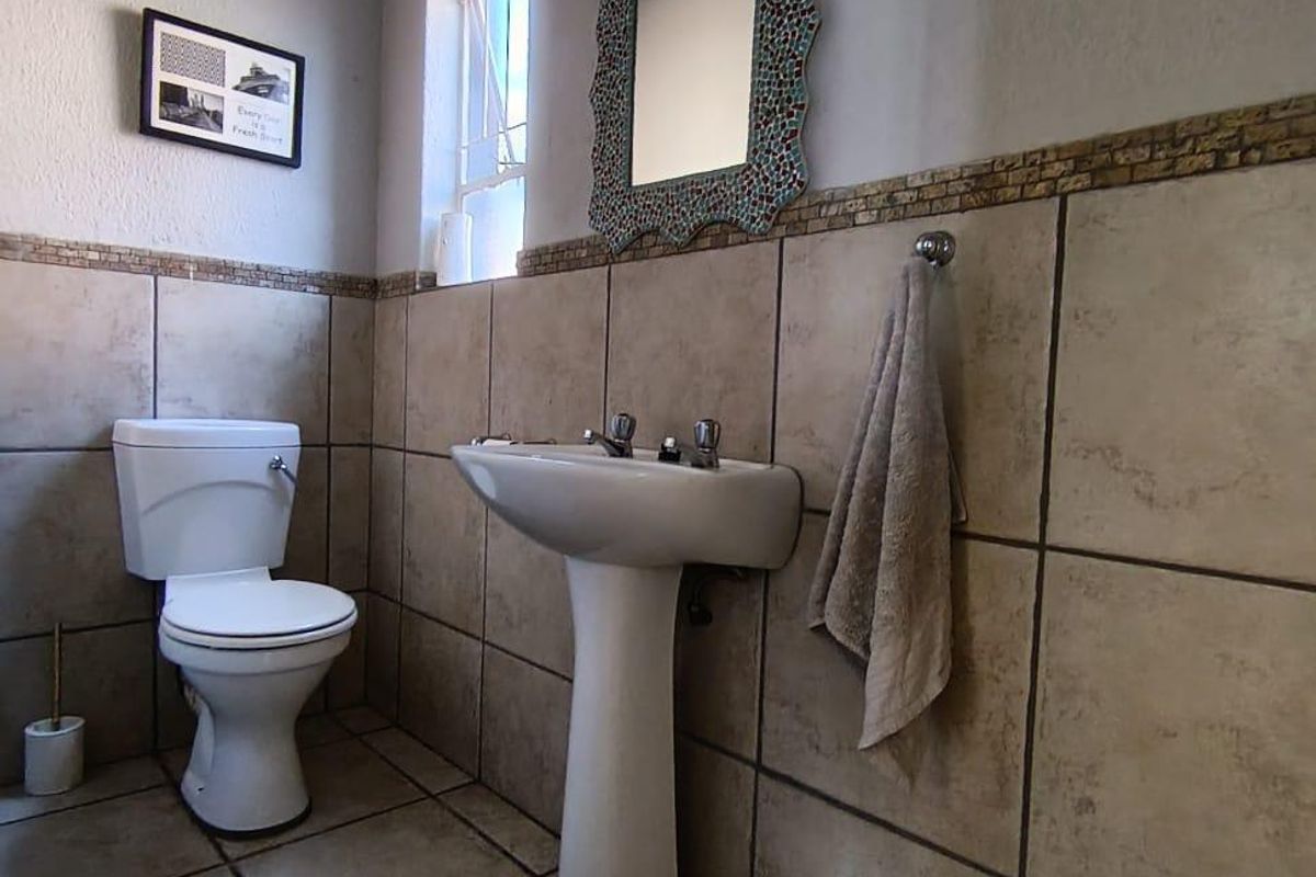 A functional bathroom featuring a pedestal basin, toilet, and neutral wall and floor tiling with a decorative mosaic border.