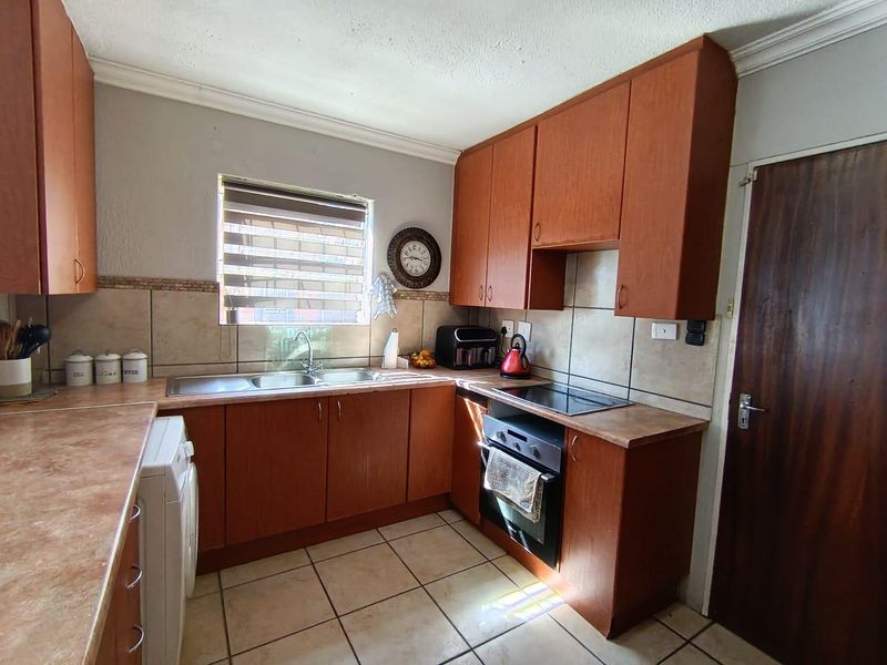 A functional kitchen featuring wood-look cabinetry, laminate countertops, a built-in oven with hob, and tiled flooring.