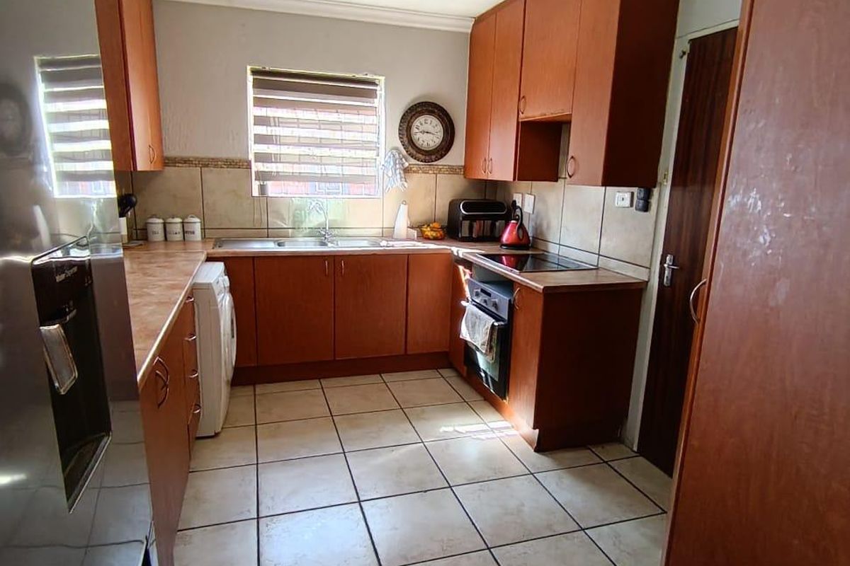 A functional kitchen featuring wooden cabinetry, laminate countertops, built-in oven, electric hob, and tiled flooring with a neutral backsplash.