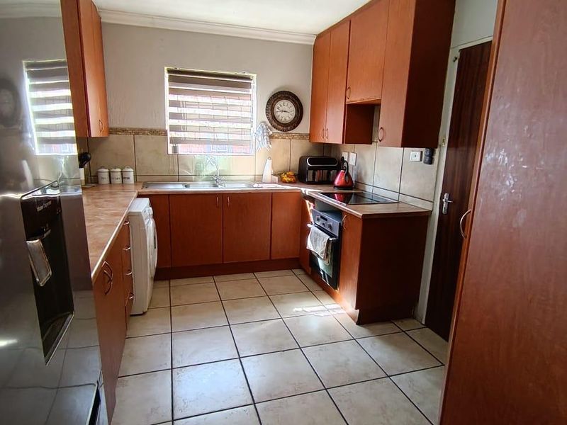 A functional kitchen featuring wooden cabinetry, laminate countertops, built-in oven, electric hob, and tiled flooring with a neutral backsplash.