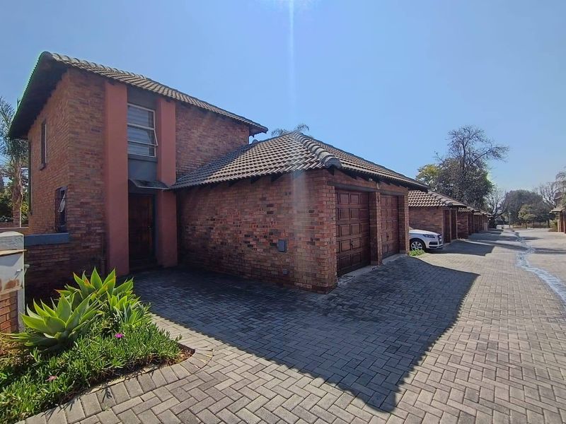 Front exterior view of a double-storey townhouse featuring a face-brick facade, tiled roof, and a paved driveway leading to a double garage.