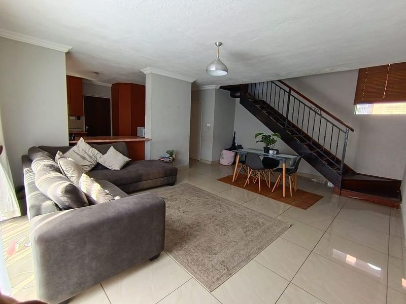 Open-plan living and dining area featuring tiled floors, a staircase with metal balustrades, and an adjoining kitchen with built-in cabinetry.