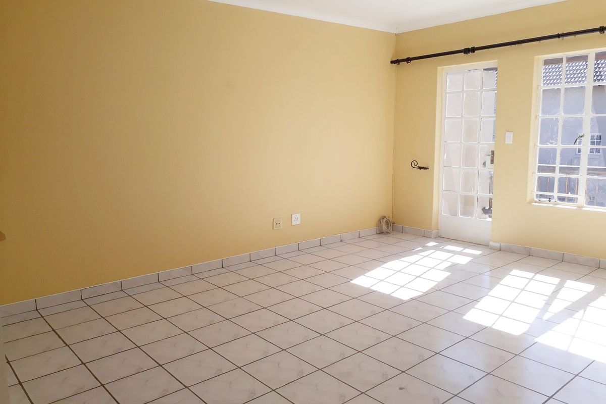 An empty living room featuring ceramic floor tiles, a glass-paneled french door, and natural light, providing a blank canvas for interior design.