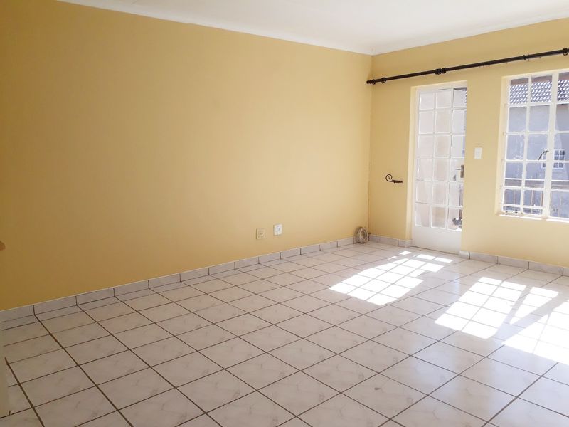 An empty living room featuring ceramic floor tiles, a glass-paneled french door, and natural light, providing a blank canvas for interior design.